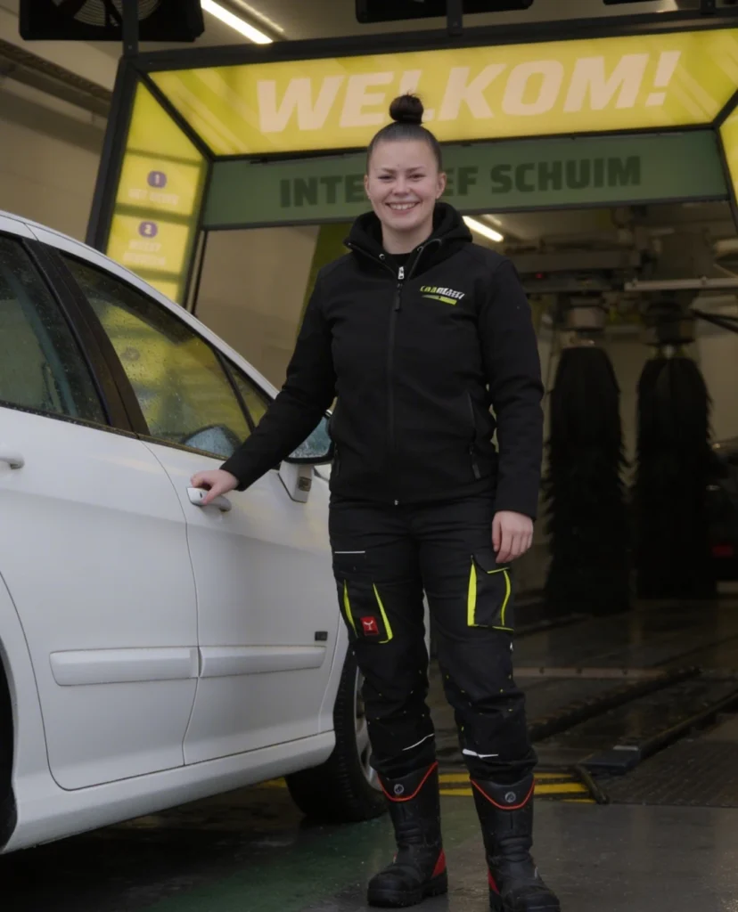 Een medewerker van Carwash Gorinchem die naast een auto staat terwijl ze aan het lachten is.